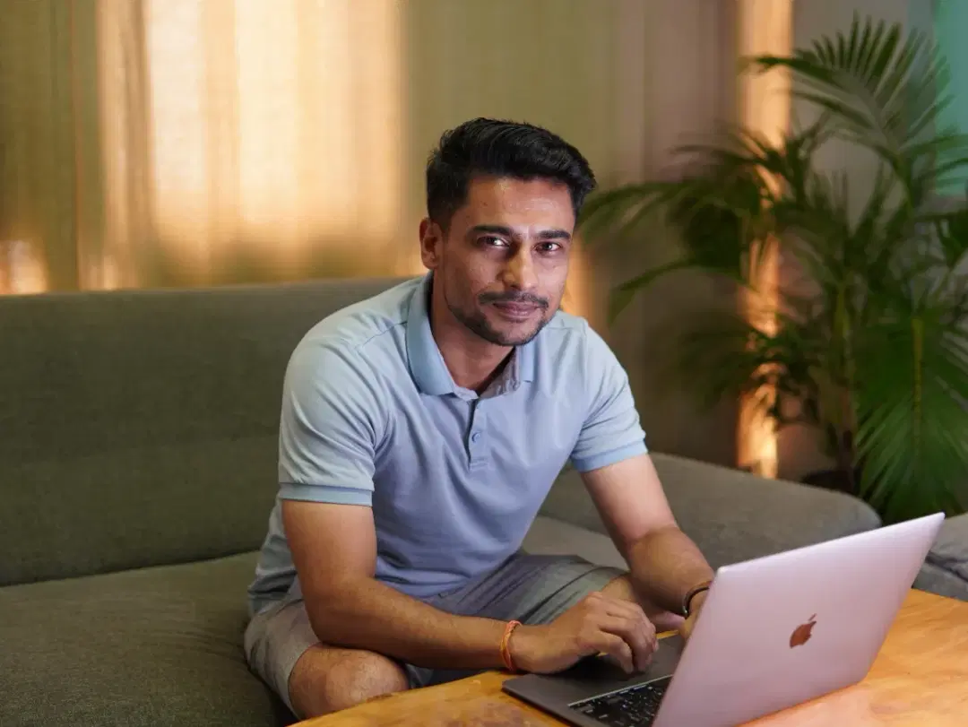 A tech expert working on a laptop at a table, making direct eye contact with the viewer.