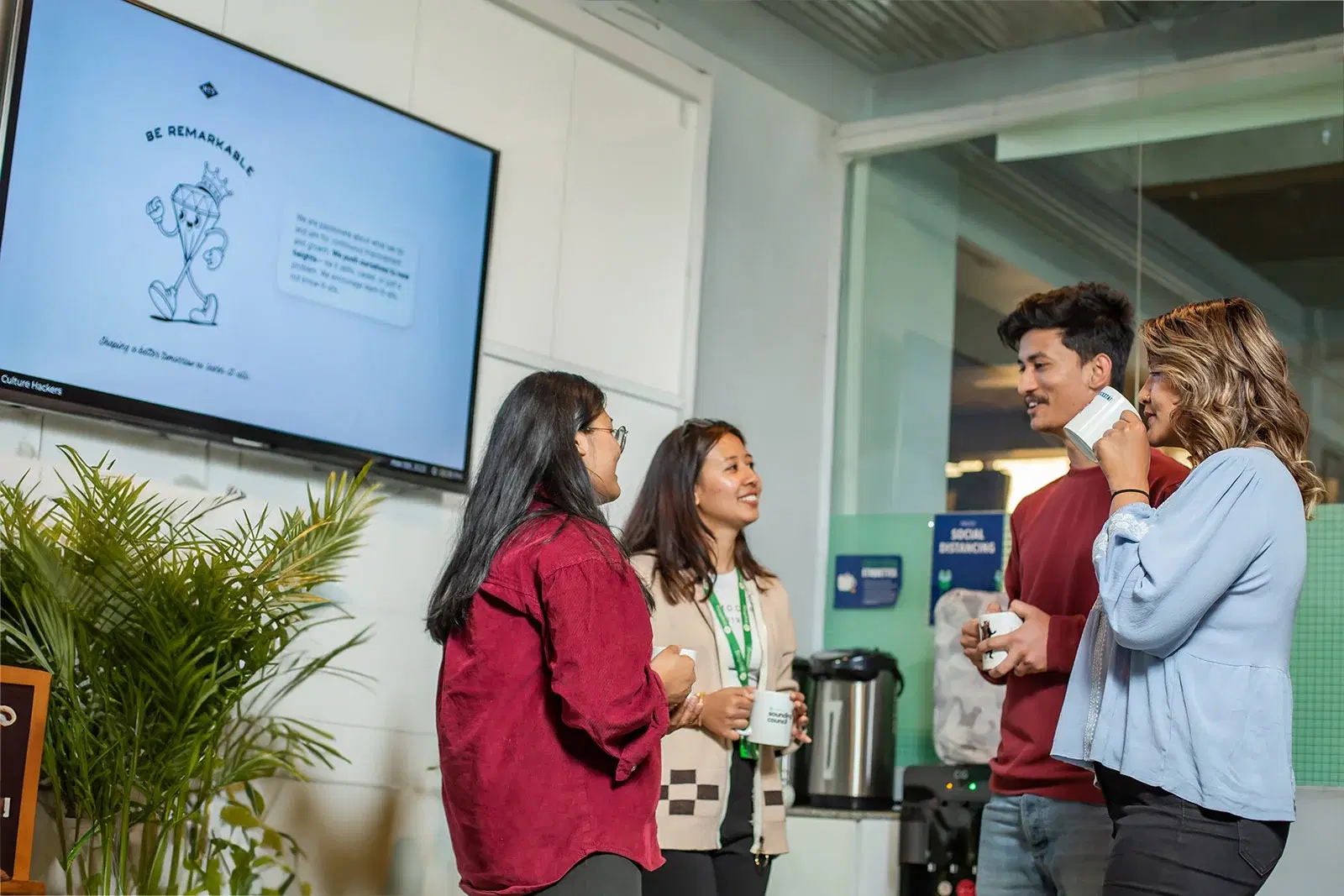 Four employees having casual coffee breaks, engaging in friendly chats at the office coffee station.